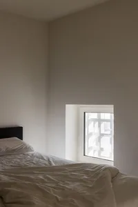 A minimalist bedroom with a white bed and textured wallpaper.