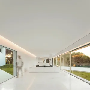 A minimalist living room with concrete walls and floors, featuring a sleek, low-slung sofa and large windows.