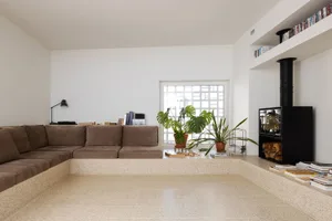 A minimalist living room featuring a light-tan floor with concrete tiles and a brown sectional sofa.