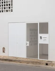 A modern building entry door with a metallic grid pattern and concrete wall in white color.