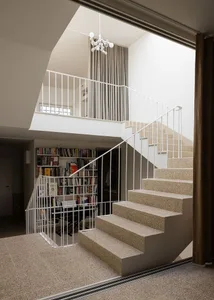 A modern interior space featuring a concrete staircase with metal railings and a bookshelf with books.