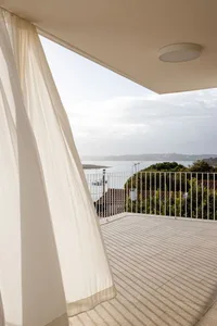 Modern interior design featuring a balcony with white curtains overlooking a scenic view of the ocean.