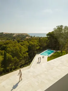 A modern residential pool deck featuring white marble surfaces, surrounded by lush greenery and an ocean view.