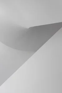 A minimalist white space with a curved wall and shadow cast on a flat surface.