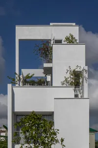 A minimalist white building made of concrete with plants on the upper levels.