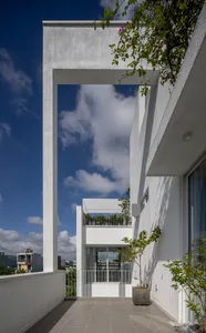 Modern exterior view of a house with a concrete balcony, white walls, and green plants.