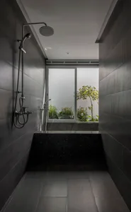 Modern bathroom with grey stone walls, metal fixtures, and a view of greenery outside through the window.