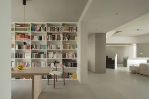 A minimalist library with light wood shelves and a wooden dining table with bananas