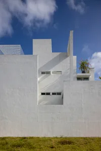 A modern, white box-shaped building constructed of concrete with a green plant growing on the rooftop.