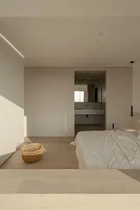 A minimalist bedroom with a wood floor, white walls, and a bed with white sheets.