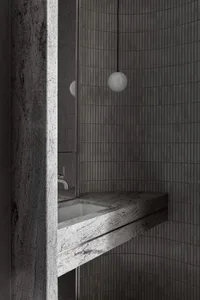 A minimalist bathroom with gray walls covered in small, vertical tiles and a granite countertop featuring a white sink.