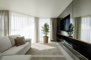 Modern minimalist living room with neutral-toned textiles, reflective surfaces, and large windows.
