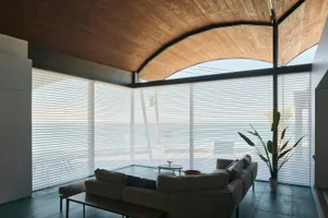 A minimalist living room featuring white blinds on large windows.
