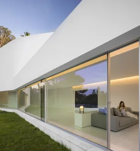 A modern house featuring glass windows and a terrace overlooking trees.