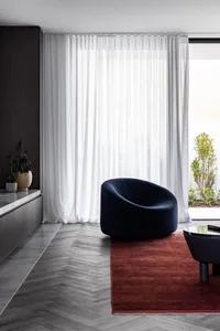 A modern living room featuring textured curtains, a marble floor, and wooden paneling.
