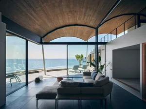 Modern living room featuring a comfortable sofa, large windows overlooking the sea, and a sleek design.