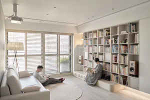 A modern living room with wooden flooring, a white sofa, and a large bookshelf filled with books.