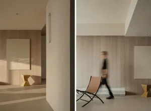 A modern living room featuring minimalist design with wooden walls, a beige chair, and abstract artwork.