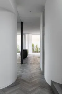 A minimalist residential interior featuring a herringbone-patterned wooden floor and white walls.