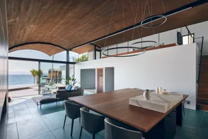 Modern minimalist living room with concrete floor and furniture, large windows with outdoor view of the sea, and minimalist d
