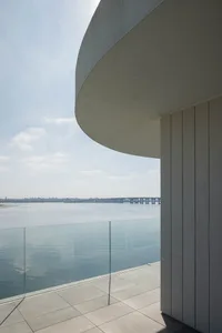 Modern residential balcony featuring concrete flooring and glass balustrade overlooking calm water.
