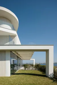 Modern residential exterior with white architectural design, glass walls, metal frame, and green grass