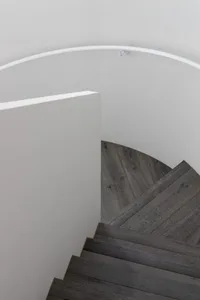 Modern wooden stairs with a white, curved wooden handrail and white walls.