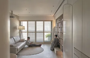 A minimalist living room featuring a white couch, glass shutters, and light wooden flooring.