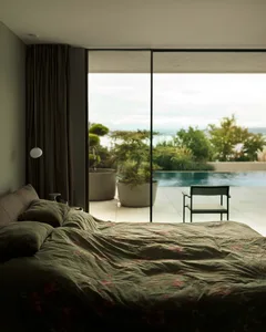 A modern bedroom featuring a dark green printed bedspread, large glass window, and outdoor patio with a pool and garden.