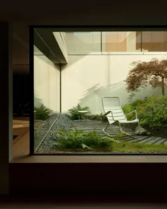 A sleek, modern lounge featuring a metal rocking chair surrounded by greenery and a small table.