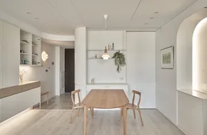 A minimalist dining room with a wooden table and chairs, white walls, and a hanging plant.