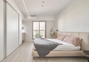 A neutral-colored minimalist bedroom with a upholstered bed, grey blanket, and pink pillows.