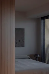 Minimalist bedroom with concrete walls, a simple bed, and a window with blinds.
