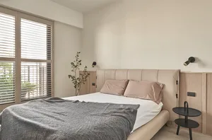 A minimalist bedroom featuring a bed with a fabric headboard, wooden furniture, and a metal bedside table.