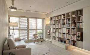 A modern minimalist living room featuring a white leather sofa, a rocking chair, and a large bookshelf filled with books.