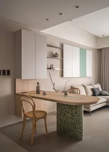 A minimalist residential living room features a wooden table with a terrazzo base, a beige sofa, and a wooden chair.