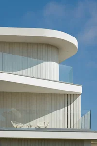 Modern balcony featuring sleek white concrete and transparent glass barriers against a clear blue sky.