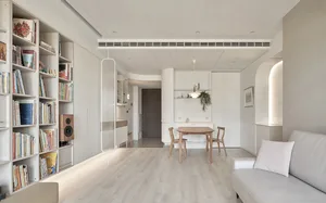 A modern living room with a white couch, wooden dining table, and bookshelf filled with books.