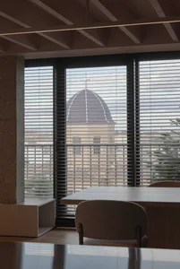 A modern room featuring metal blinds, a concrete column, and a wooden floor.