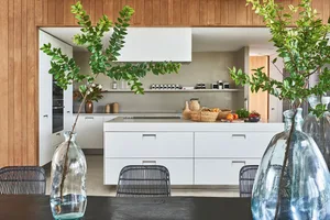 A modern kitchen features white cabinets, wooden countertops, and a central island equipped with a sink and various decorativ