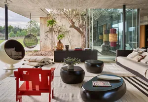 A modern living room with a red chair, black coffee tables, and a hanging chair outside.