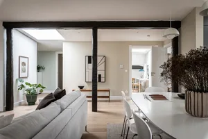 A modern living room featuring light wood flooring and white walls, with a comfortable seating area, dining table, and minima