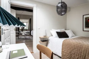 A minimalist bedroom with a bed featuring a textured brown blanket and white sheets, alongside a wooden chair and a green not