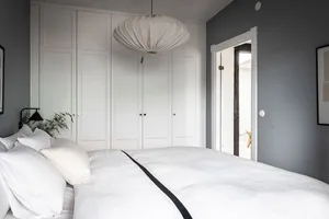 Modern, minimalist bedroom with white bedding, large window, and large white wardrobe.