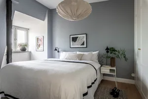 A minimalist bedroom with a white bed, white walls, and a wooden floor.