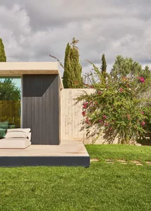 A minimalistic house with a concrete patio and greenery in the background.