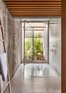Modern bathroom with minimalist design featuring concrete walls and a glass door leading to an outdoor patio area.