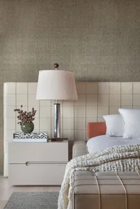 A modern bedroom featuring a leather headboard with a silver lamp and a blanket on the bed, set against a neutral-colored wal