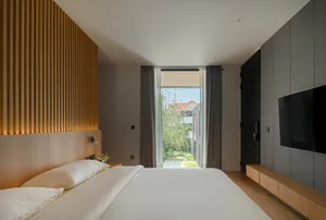 Clean and minimal bedroom with a bed, window, and wooden headboard.