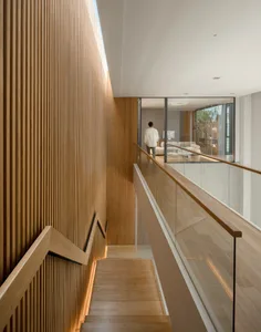 A modern residential interior with a wooden floor and walls, featuring a glass railing.